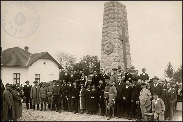 Historijska fotografija iz 1930. godine koja prikazuje grupu ljudi okupljenih oko spomenika posvećenog svim verama u Čačku, sa simbolima različitih religija urezanim na spomeniku