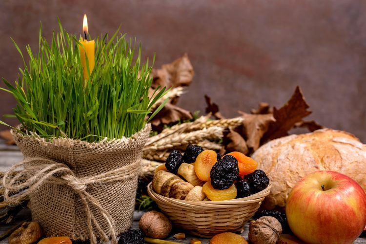 Tradicionalna srpska božićna scena sa zelenim pšenicom, zapaljenom svećicom, suvim voćem, orasima, jabukom, hlebom i jesenjim lišćem na rustičnom drvenom stolu."